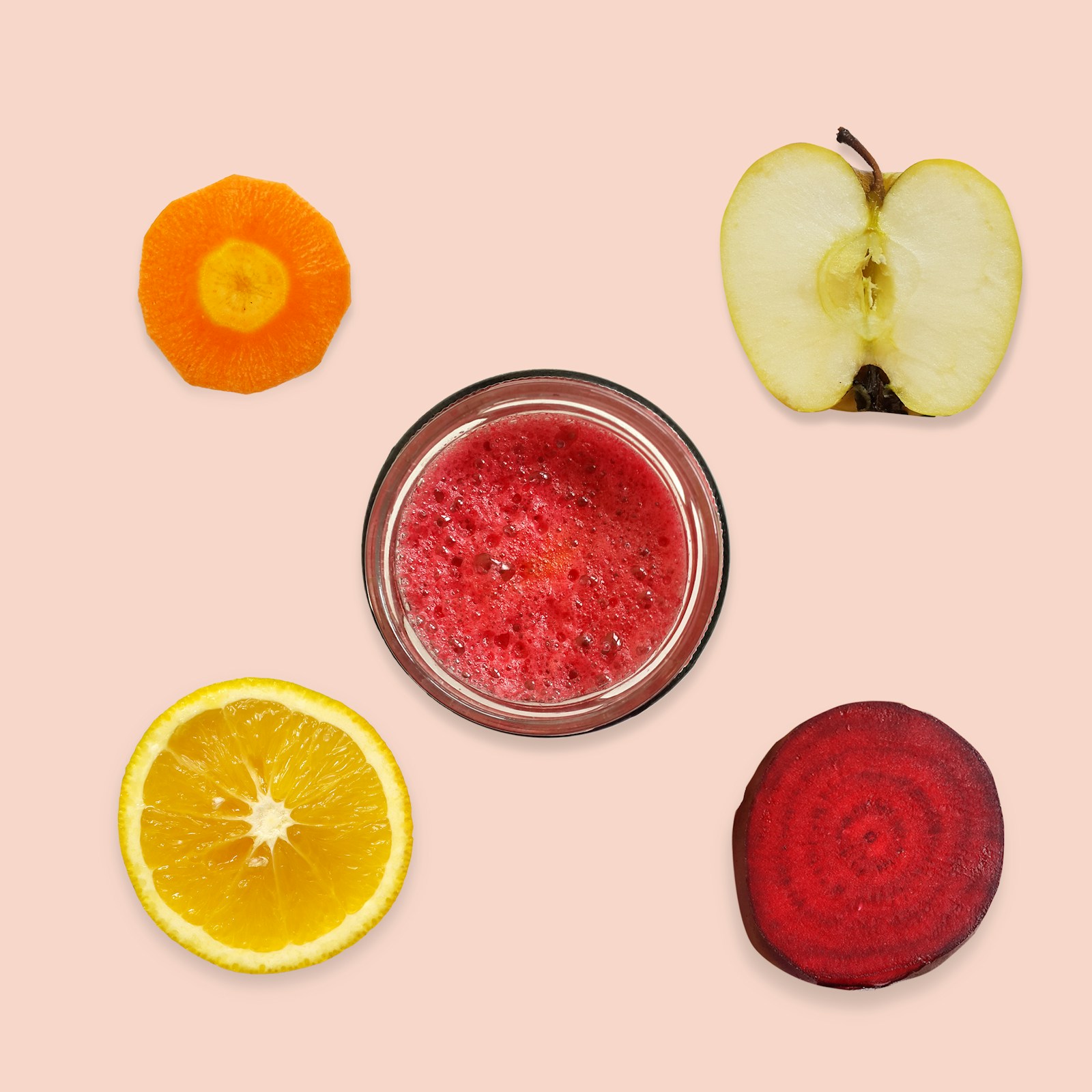 Glass med friskpresset juice omgitt av gulrot, eple, appelsin og rødbet