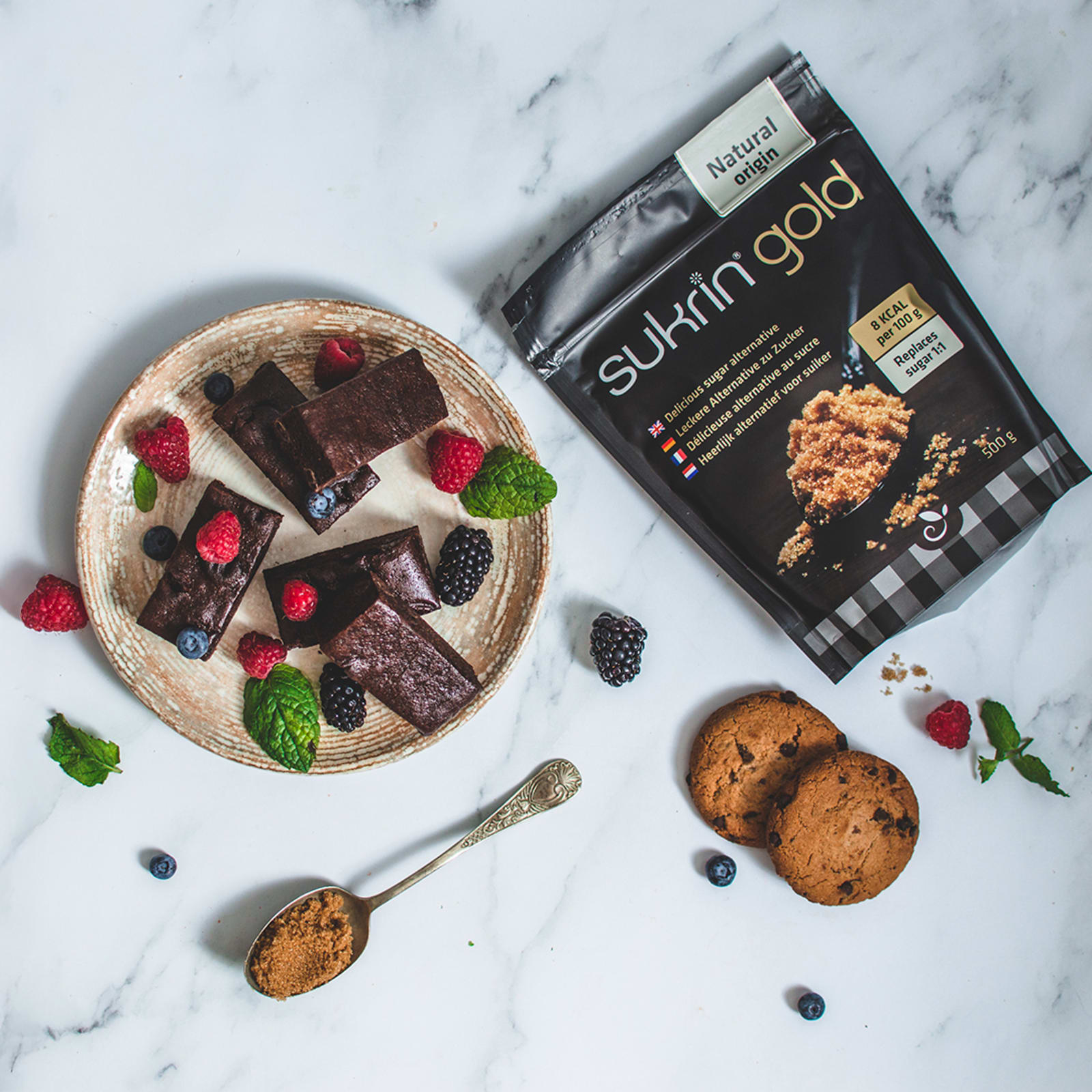 Sukrin Gold ved siden av brownies med bær og kjeks på marmor